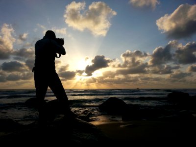 Person Capturing Photo Near Sea Under Clear Blue And White Cloudy Sky During Daytime