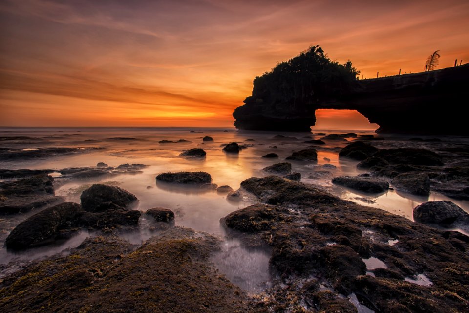 Orange And Yellow Sunset Skies Over Grey Seashore Rocks And Calmed Ocean