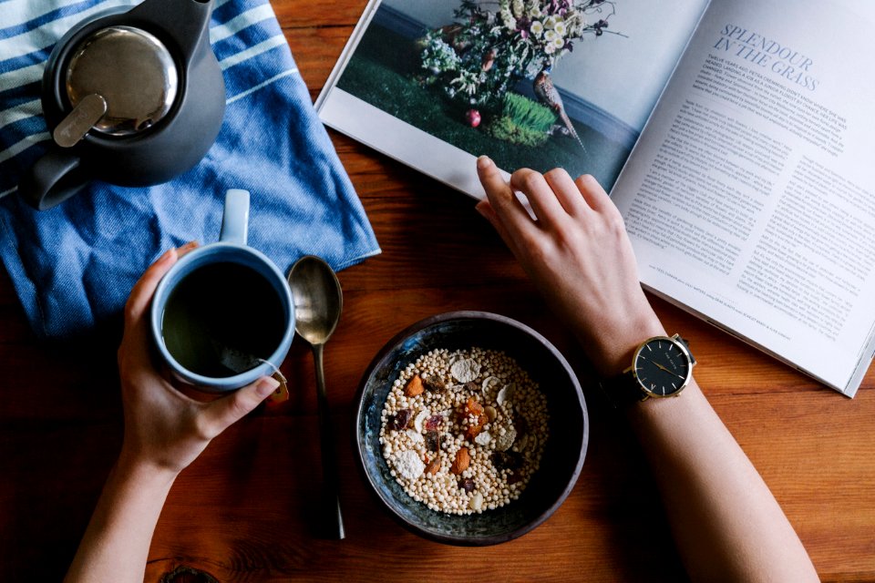 Person Holding White Ceramic Coffee Cup Leaning On Brown Wooden Table