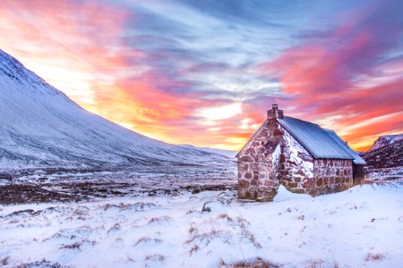 Brown House Surrounded By Snow Covered Field Near Snow Covered Mountain Under Yellow Blue And Orange Sunset photo