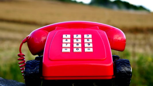 Red Rotary Phone With Black Wheels Near Brown Grasses During Day Time photo