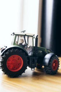 Black And Green Farm Tractor Toy On Brown Wooden Table Beside Window photo