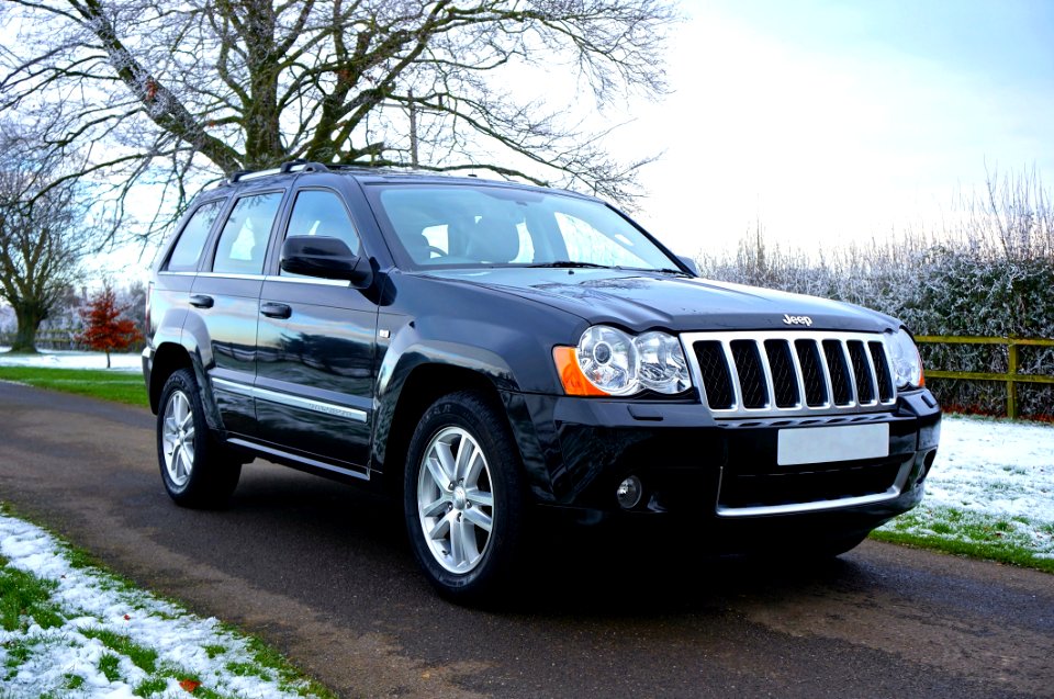 Black Jeep Suv On Black Asphalt Road Near On Snowy Grass Lawn