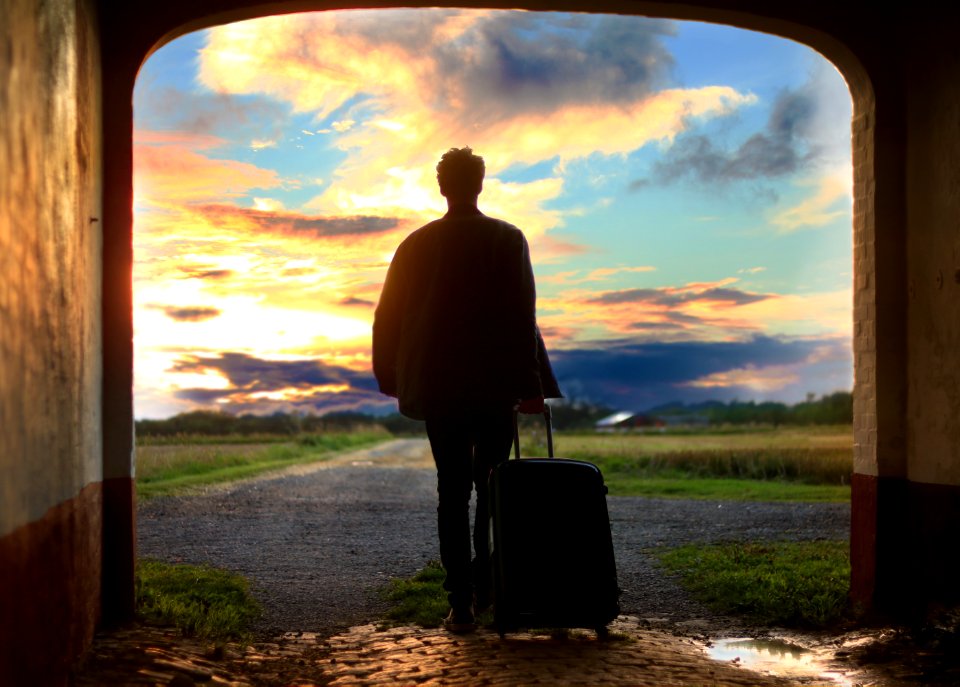 Man Pulling Luggage Walking Near Gray Concrete Road During Sunset
