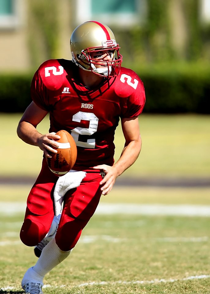Football Player With Ball Running On Green Field During Daytime