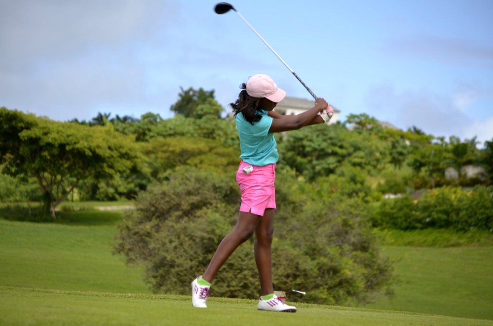 Woman In Green Polo Shirt And Pink Shorts Playing Golf Under Grey And Blue Skies During Daytime