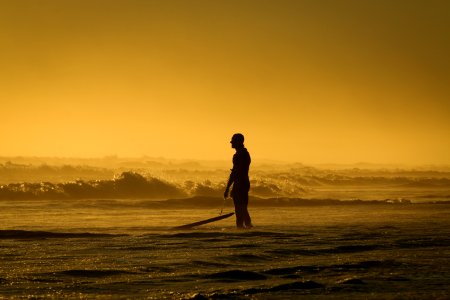 Man Standing On Seashore While Holding His Surfing Board During Sunset photo