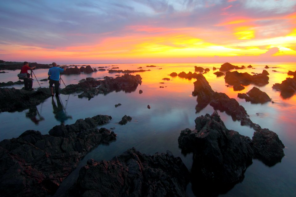 2 People Standing On Rock Formation Reflected On Water During Sunset