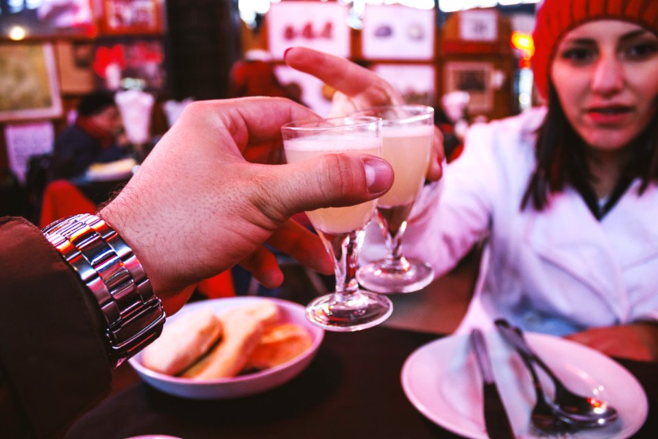 Man Wearing Silver Link Watch Holding A Glass Containing White Liquid In Front Of A Woman
