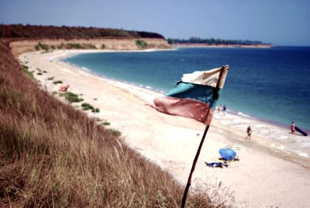Blue Ocean Near On White Sands With White Blue And Red Flag On Shore photo