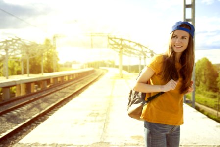 Smiling Woman In Orange T Shirt And Blue Snap Back Cap Carrying Backpack