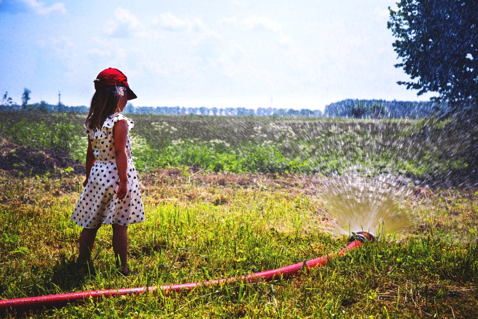 Girl On Green Grass Near Red Hose While Pumping Water During Daytime
