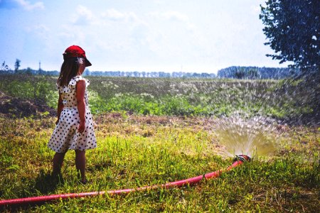 Girl On Green Grass Near Red Hose While Pumping Water During Daytime photo