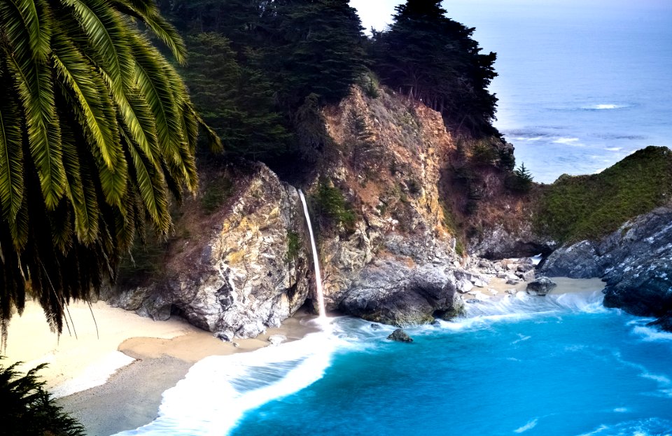Blue Sea Near Brown And Grey Rock With Green Leaf Trees