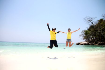 Woman In Blue Denim Mini Short Smiling While Holding Another Person In A Jump Shot Photo At Seashore During Daytime photo