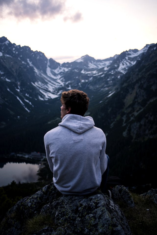 Man Wearing White Hoodie Sitting On A Rock With A View On Mountain photo