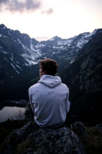 Man Wearing White Hoodie Sitting On A Rock With A View On Mountain photo