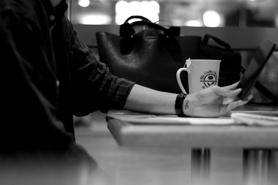 Gray Scale Photograph Of Person Sitting Beside Black Leather Bag photo