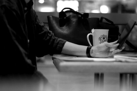 Gray Scale Photograph Of Person Sitting Beside Black Leather Bag