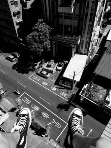 Grayscale Photography Man Wearing All Star Converse High Tops Below In Street And Building photo