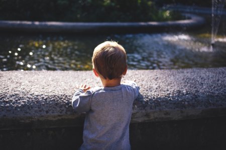 Boy In Gray Top Standing In Front Of Water Fountain photo