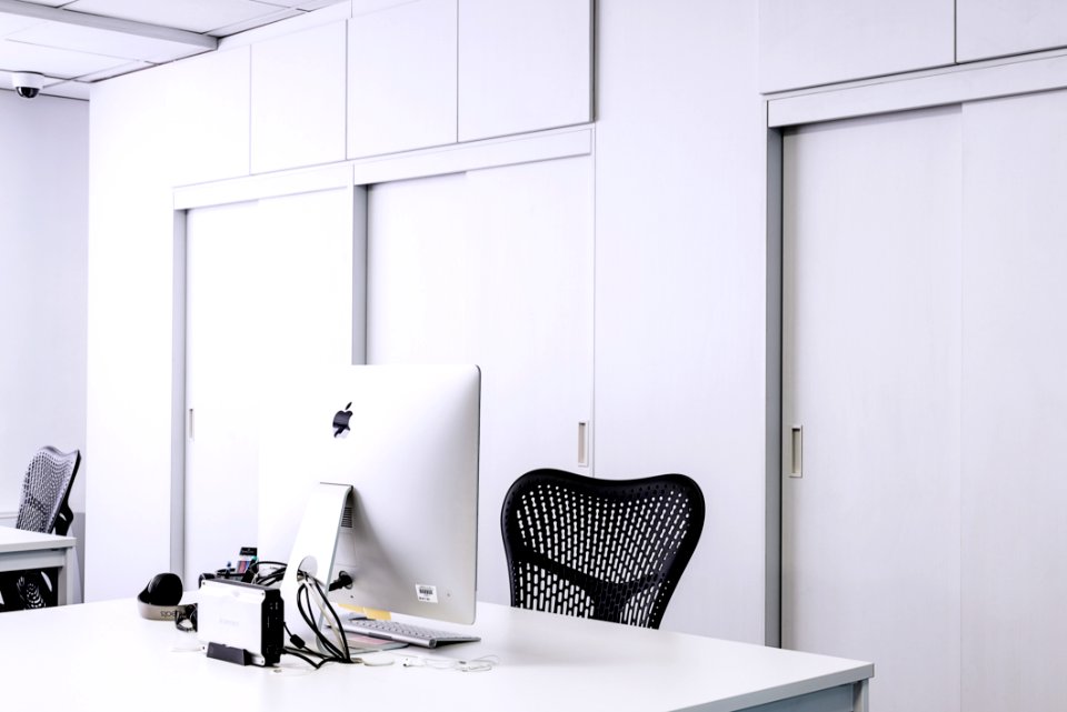 Black Mesh Office Rolling Chair Beside White Wooden Desk With White Imac