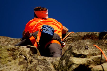 Person In Orange Shirt Climbing Rock During Daytime