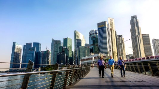 Three Men Walking On Bridge In Front Of High Rise Buildings At Daytime photo