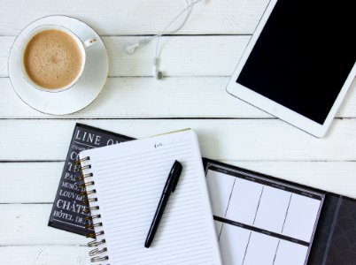 Black Pen On White Writing Spring Notebook Between White Ipad And White Ceramic Mug With Latte On White Plate photo