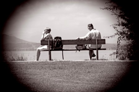 Man Sitting On Other Edge Of Bench Parallel To Woman With Bags In Between Them