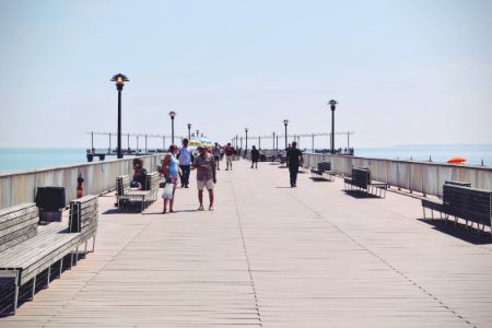 People Walking On A Beige Concrete Bridge Pathway Near Seashore During Daytime