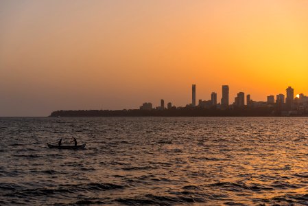 2 Person On The Boat On The Ocean In Front Urban City During Golden Hour