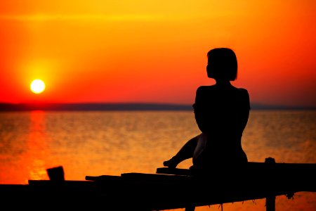 Silhouette Of Woman Sitting On Dock During Sunset photo