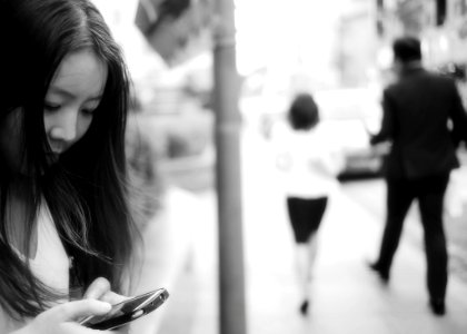 Woman Using Smartphone At Sidewalk Near Man And Woman Walking Away From Her photo