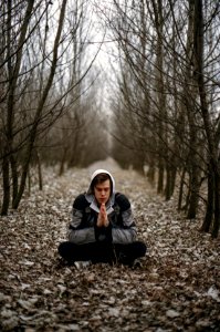 Man Wearing Gray Black Zip Hoodie Jacket Praying In Between Black Tree During Daytime photo