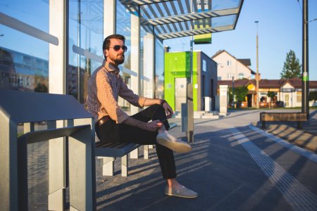 Man Wearing Sunglasses Sitting At Bus Stop During Daytime