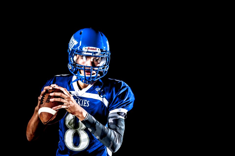 Man Holding Football And Football Uniform In Black Background