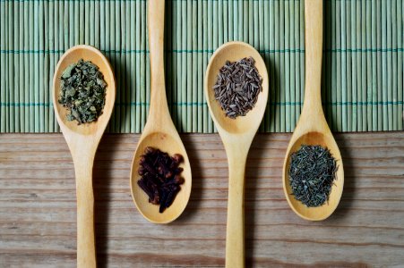 Brown Wooden Spoon With Herbs On Top Of Green Bamboo Mat And Brown Wooden Surface photo