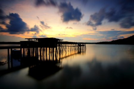 Silhouette Of Wooden House And Walkbridge On Water