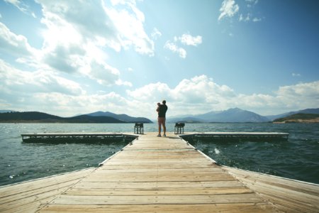 Person Standing On Brown Wooden Dock Under Clue Sky During Daytime photo