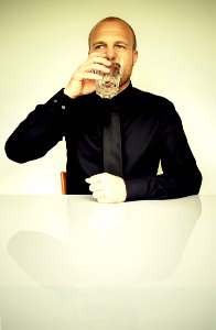 Man In Black Dress Shirt Sitting In Front Of White Table Drinking Water photo