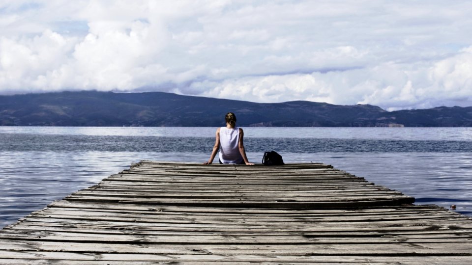Person Sitting On Brown Wooden Dock Under Cloudy Blue Sky photo