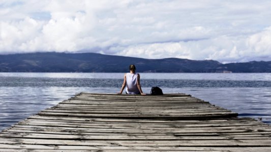 Person Sitting On Brown Wooden Dock Under Cloudy Blue Sky