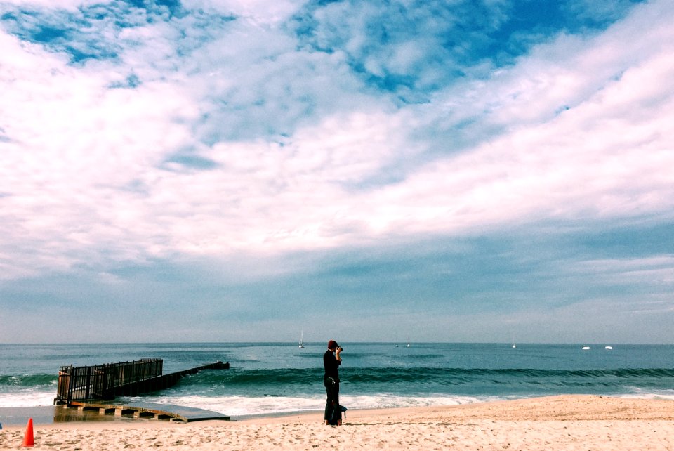 Person In Black Top Standing On Seashore Under White Clouds