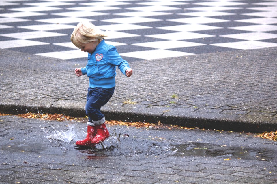 Boy In Blue Jacket Hopping On Water Puddle