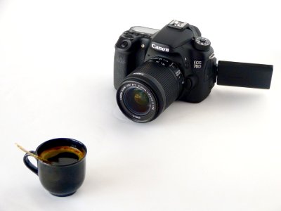 Black Canon Dslr Camera In Front Of Coffee In Black Ceramic Teacup photo