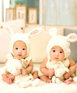 2 Babies Wearing White Headdress White Holding White Plush Toys photo