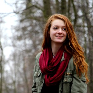 Woman In Green Zip Up Cargo Jacket And Red Scarf Smiling Sideways