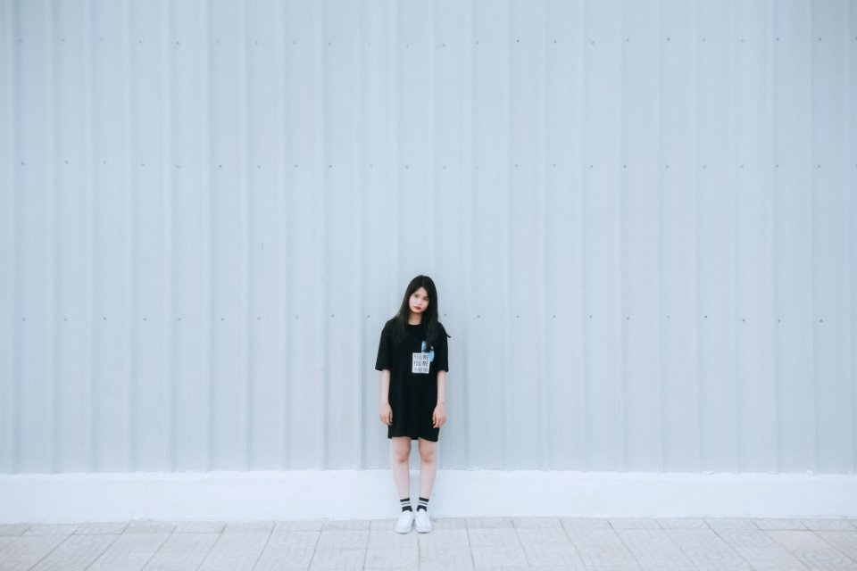 Woman In Black Elbow Sleeve Shirt And Black Shorts Standing Behind White Wall
