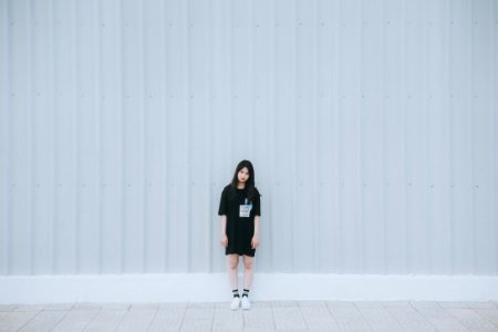 Woman In Black Elbow Sleeve Shirt And Black Shorts Standing Behind White Wall photo